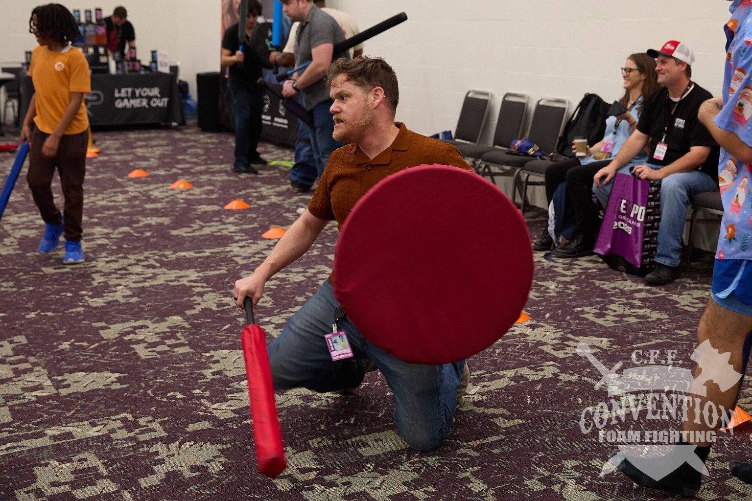 A participant kneels with a red foam shield and weapon.