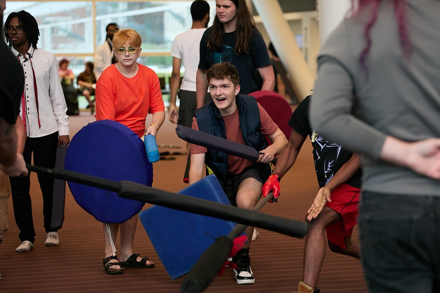 A mixed group of fighters advance into a foam battle with shields and swords.